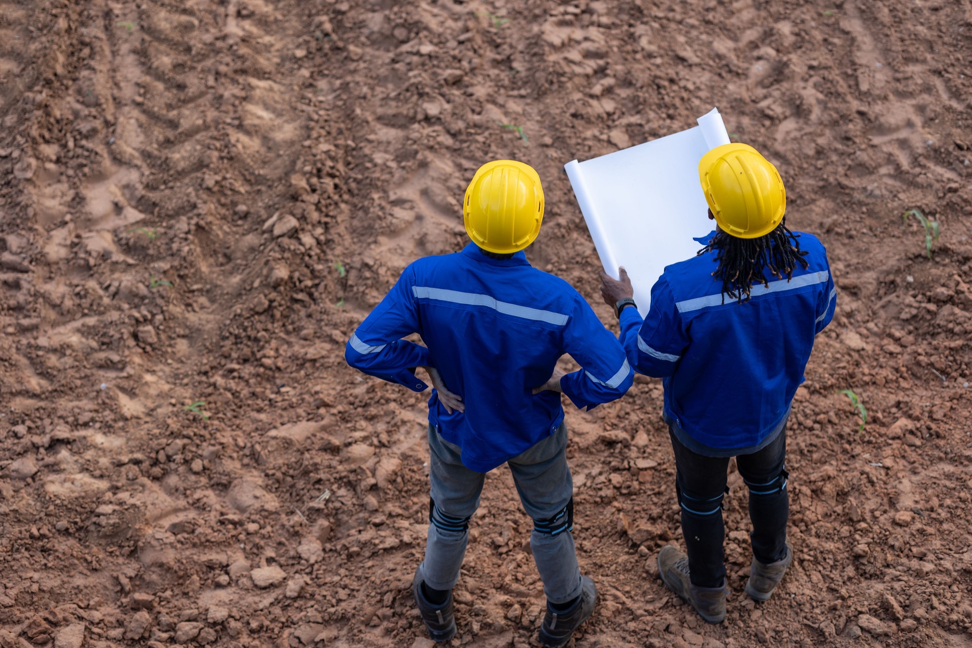 Land surveyor team standing working together at construction field consult study looking building location with floor plan